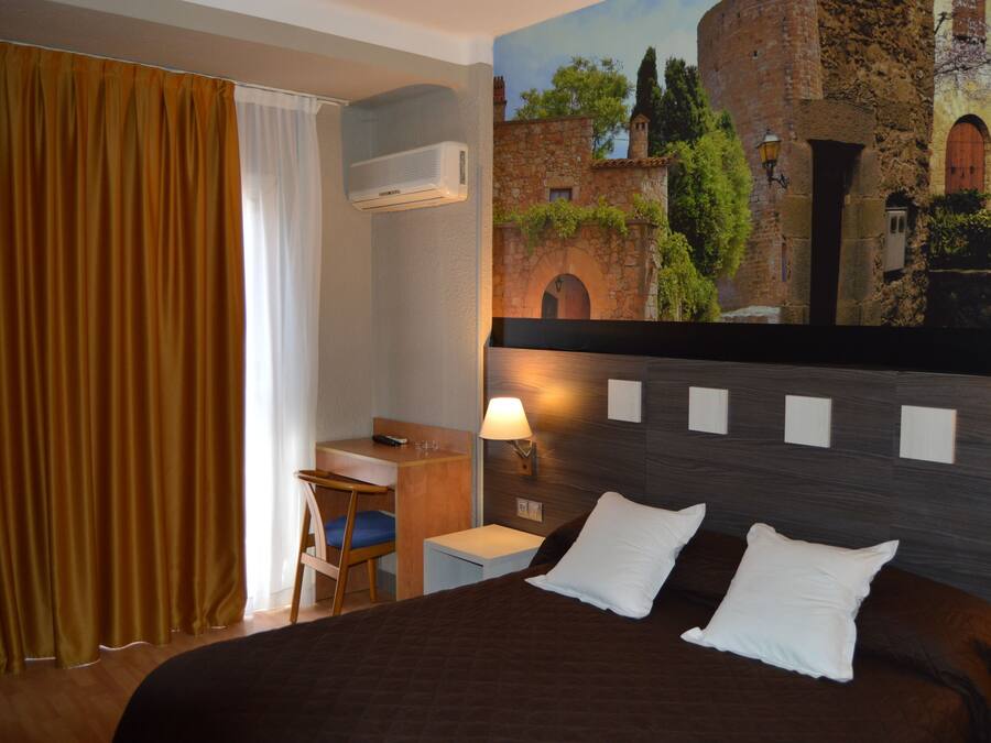 A hotel room with a bed, a desk, a chair, and a wall-mounted air conditioner.