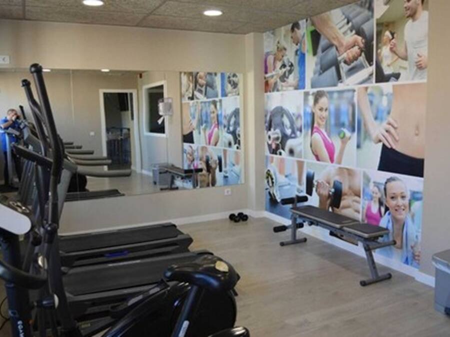 Un gimnasio con equipamiento de ejercicio, un espejo grande y una pared decorada con imágenes relacionadas con el fitness.