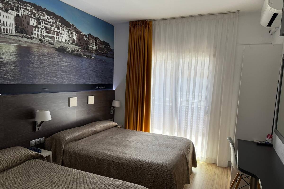 A hotel room with two beds, a large window with curtains, a wall-mounted TV, and a painting of a coastal town.