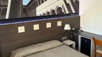 Een hotelkamer met een bed, een bureau, een stoel, een lamp en een koelkast.