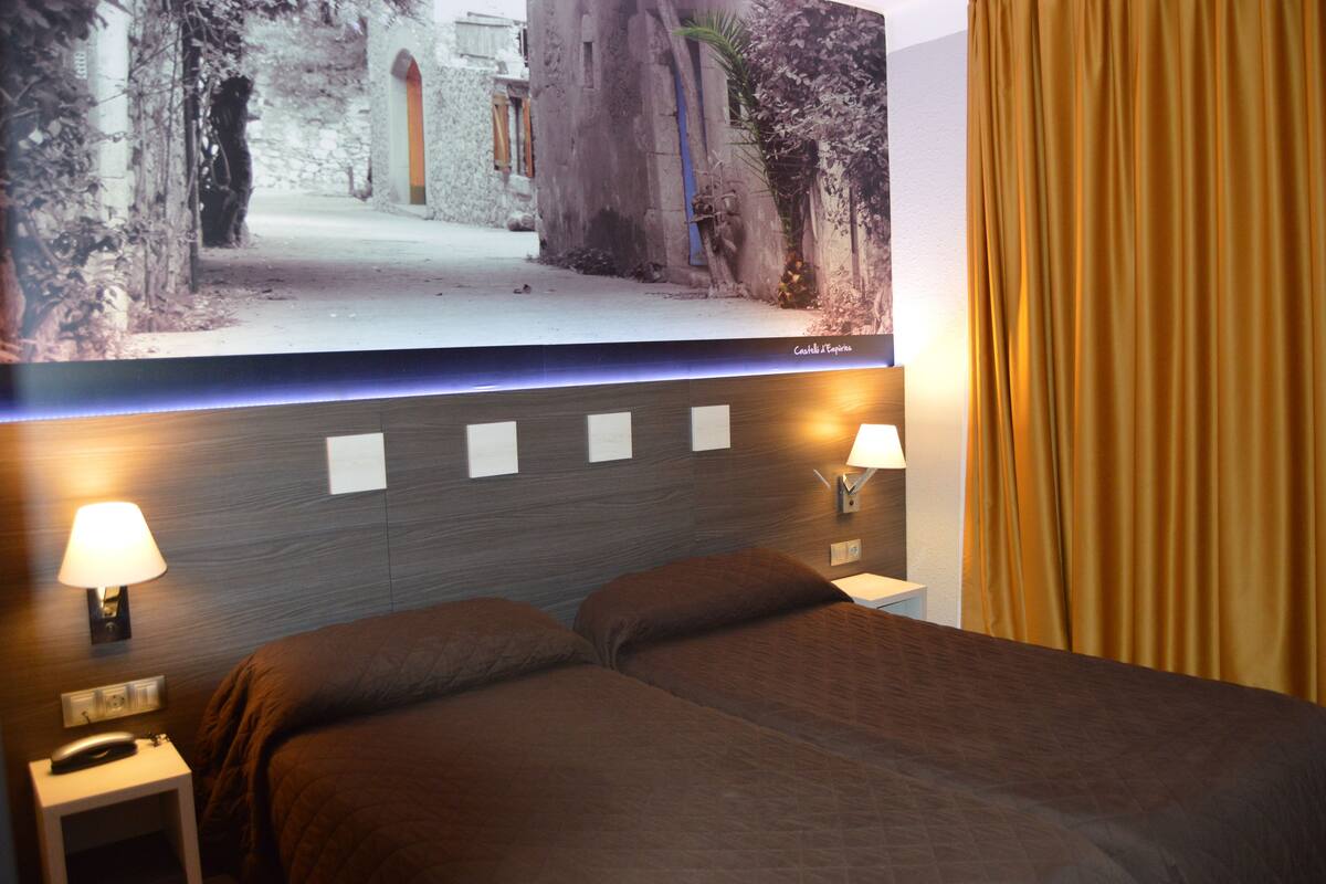 A hotel room with a bed, two bedside lamps, a wall-mounted TV, and a curtain.