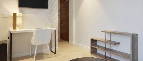 A modern room with a desk, chair, TV, and a wooden shelf unit.