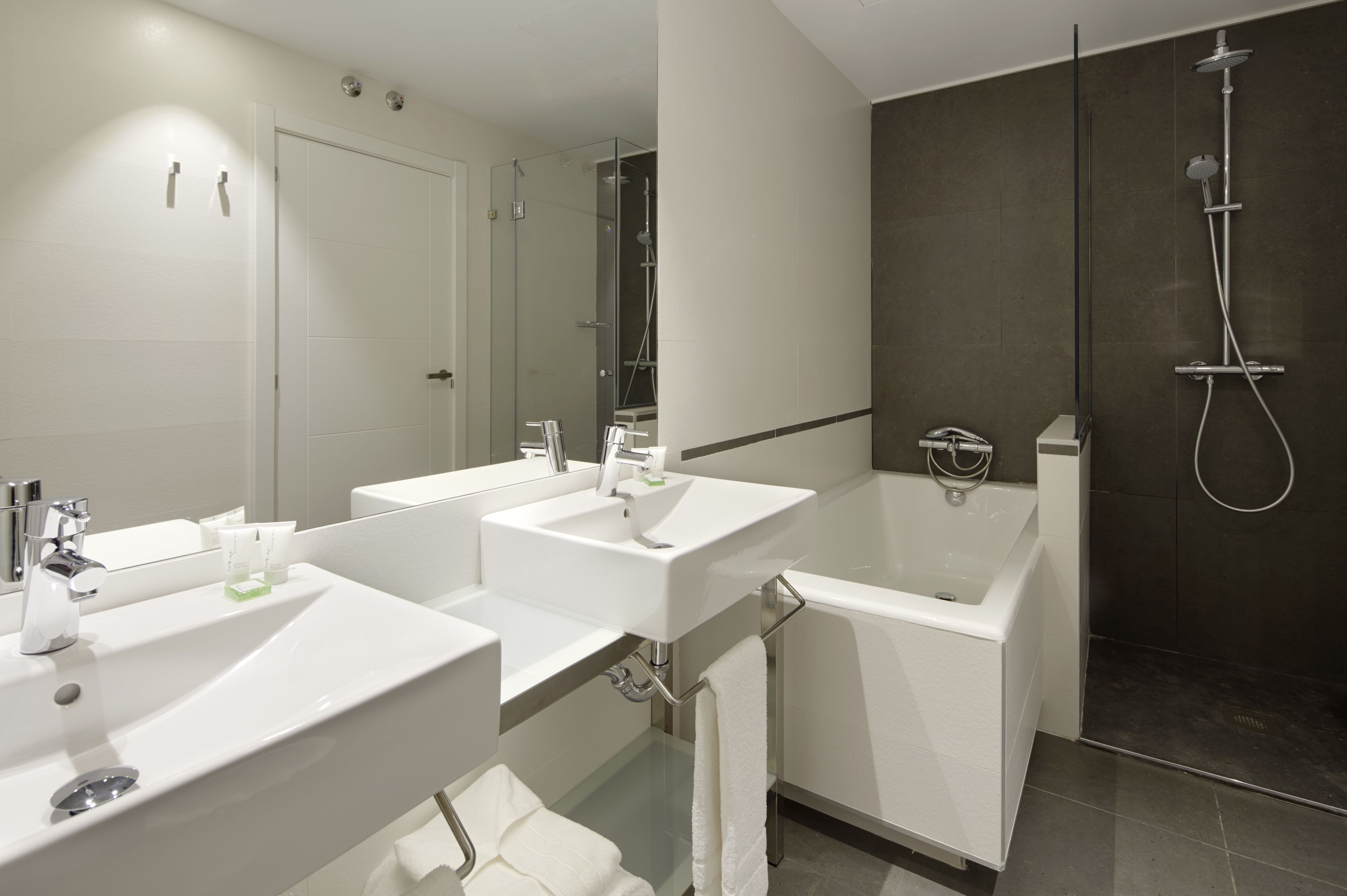 A modern bathroom with two sinks, a bathtub, and a glass-enclosed shower.