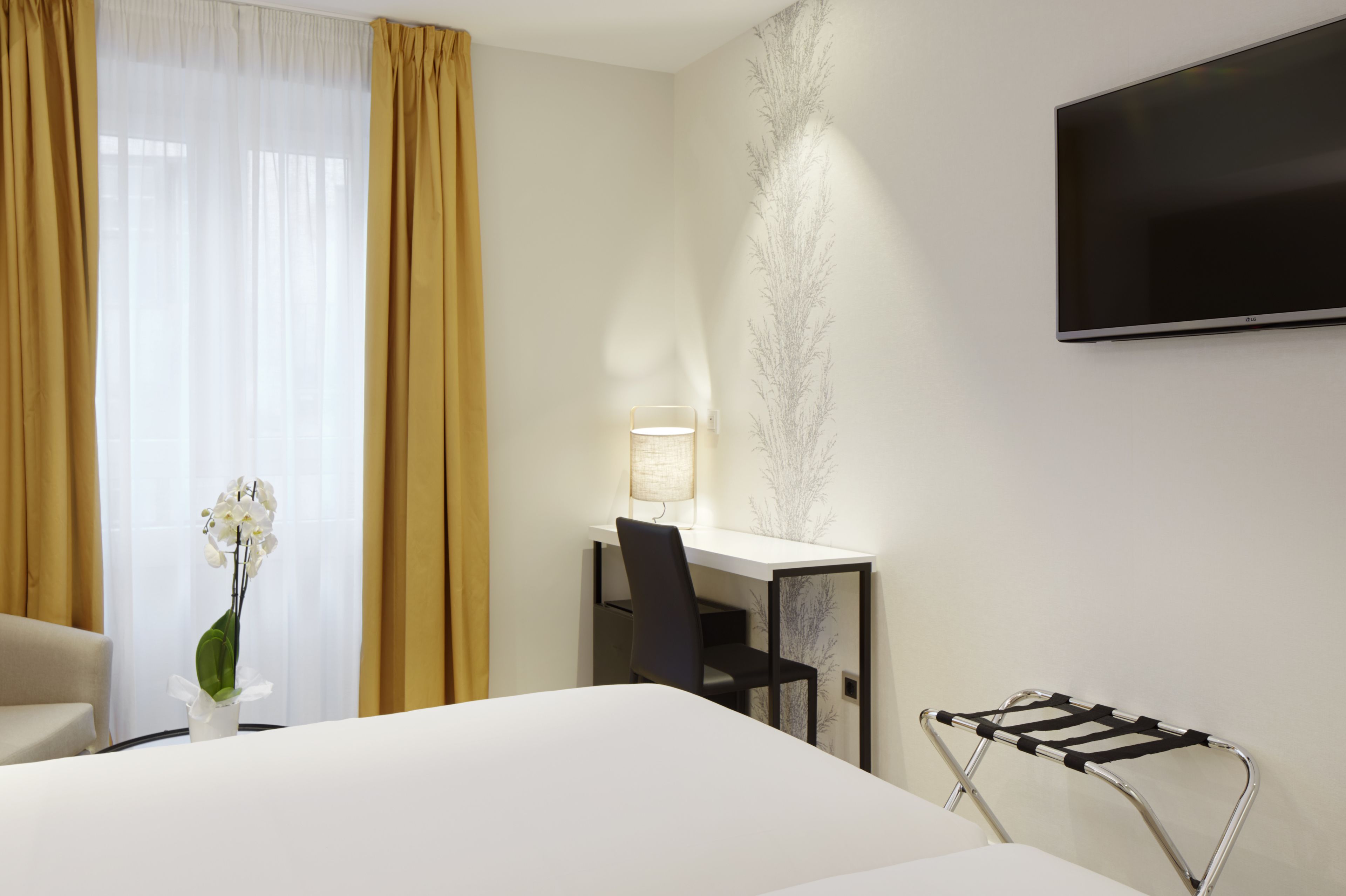 Habitación de hotel con cama, escritorio con silla, televisor montado en la pared y radiador.