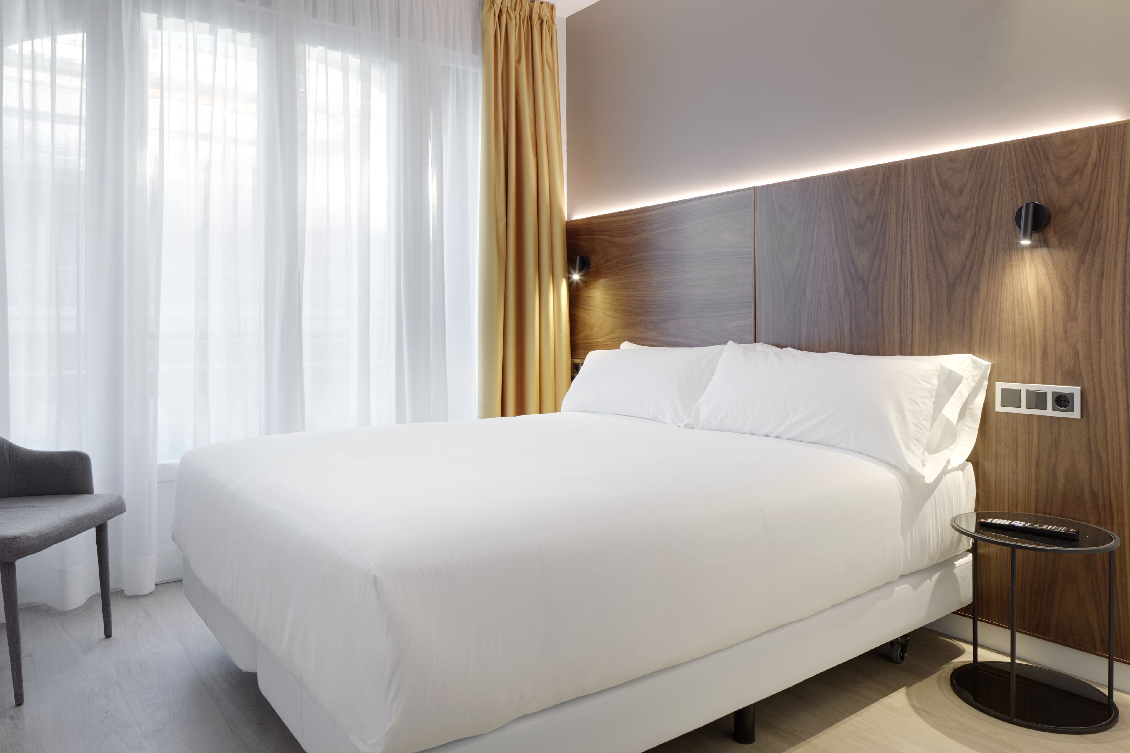 A modern hotel room with a large bed, a small side table, and a chair.