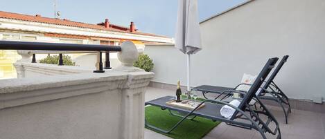 A balcony with a table, two lounge chairs, a bottle of champagne, and a white umbrella.