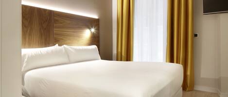 A modern hotel room with a large bed, a wooden headboard, a flat-screen TV, and a large window with yellow curtains.