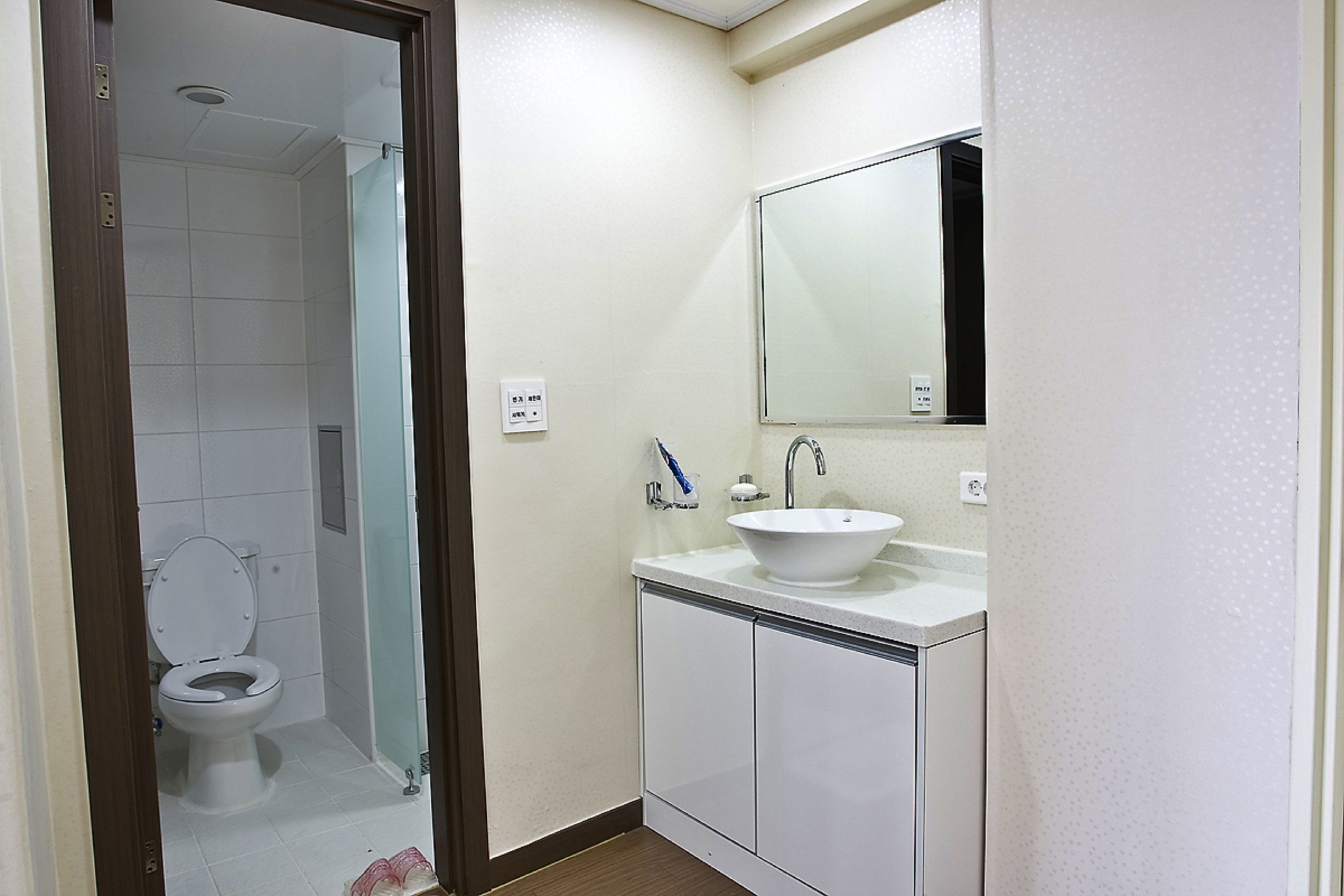 A bathroom with a toilet, sink, mirror, and cabinet.