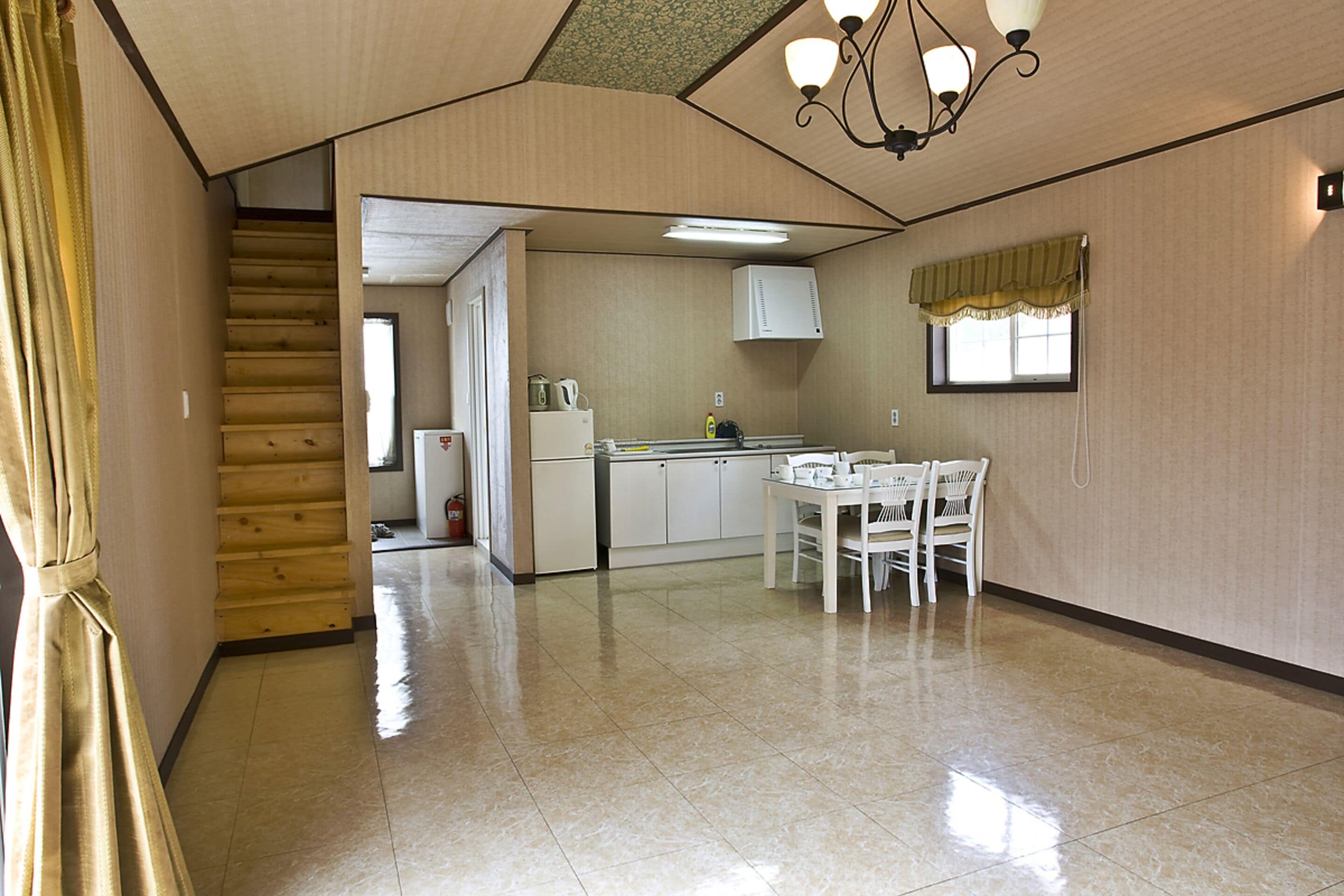 A spacious kitchen with a dining area, wooden staircase, and a chandelier.