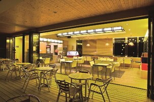 An indoor dining area with tables and chairs, a wooden ceiling, and a view of the outside through large windows.