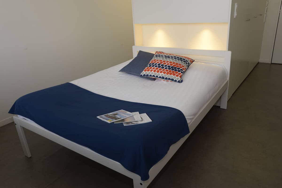 Ein ordentlich bezogenes Bett mit blauer Bettdecke, einem gemusterten Kopfkissen und einer Zeitschrift auf dem Bett.