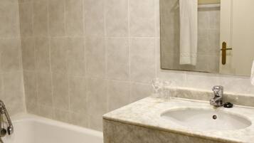 Un baño con bañera, lavamanos, espejo y un taburete pequeño.