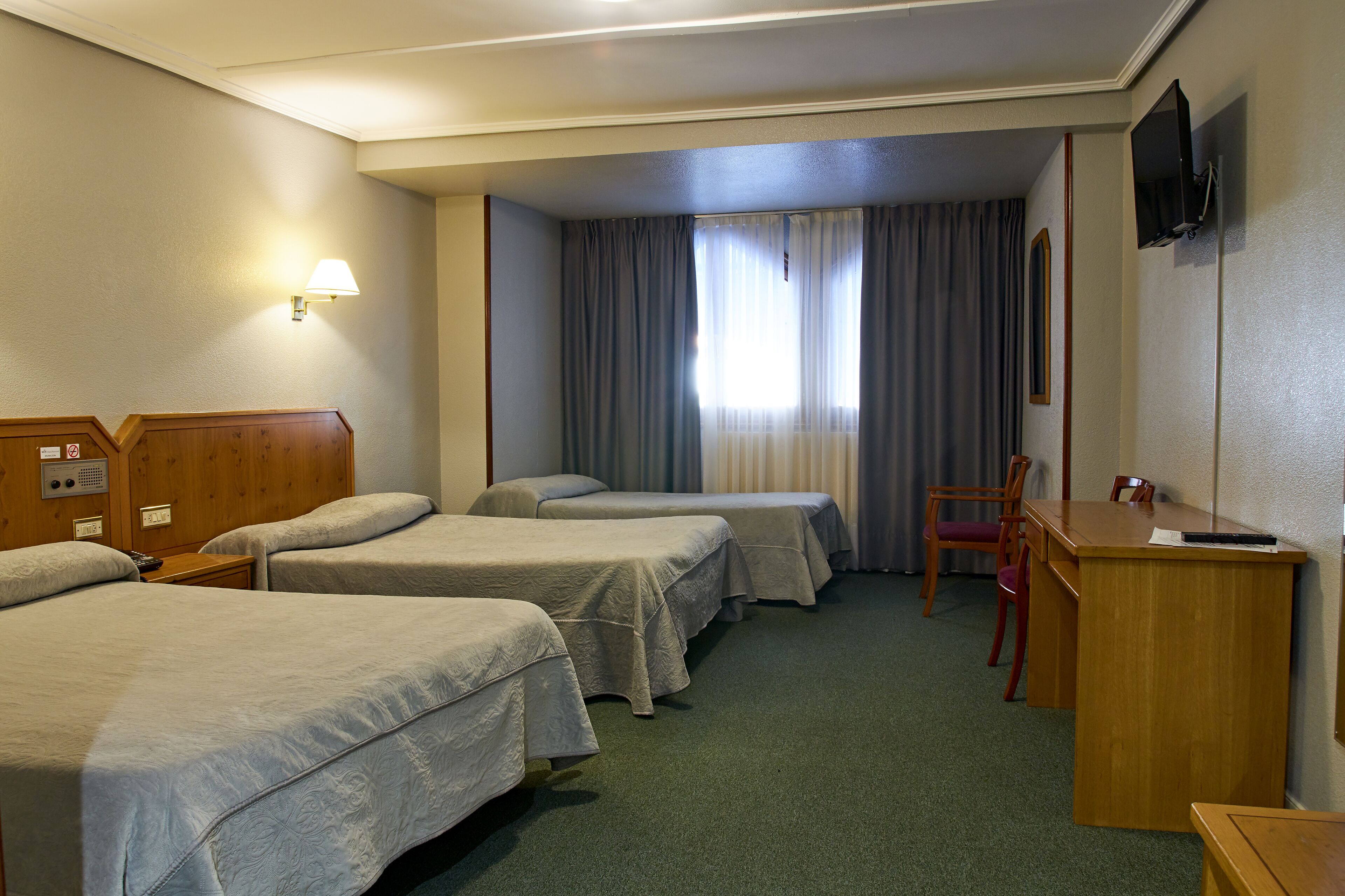 Une chambre d’hôtel avec trois lits, un bureau, une chaise, une télévision et une lampe.