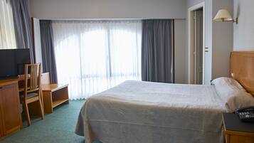 Una habitación de hotel con cama, escritorio, silla, televisor y lámpara.