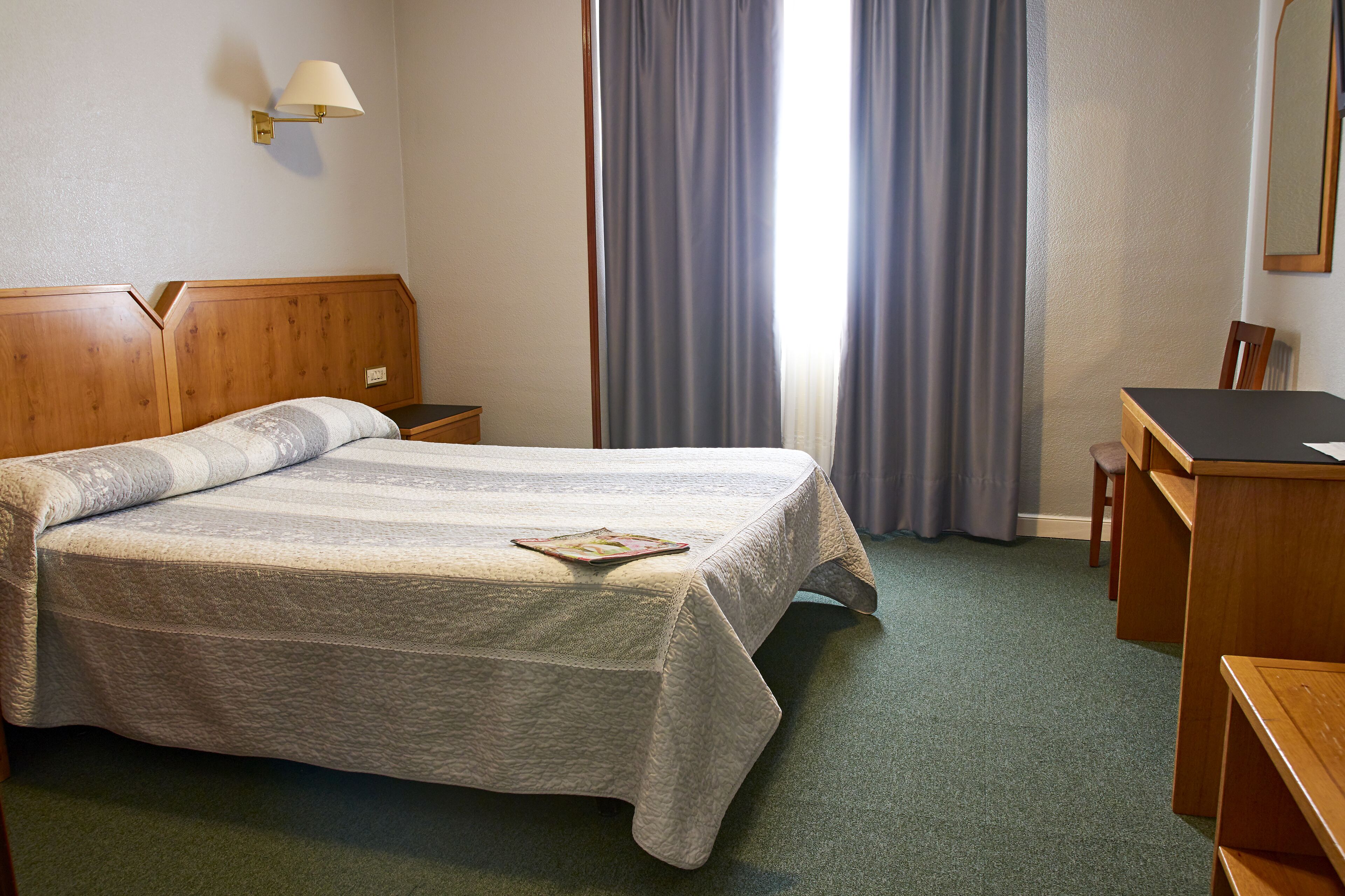 Een net opgemaakt bed met een gestreept dekbedovertrek, een bedlamp en een houten nachtkastje.