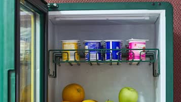 A small refrigerator with a green door, containing fruits, yogurt, and other food items.
