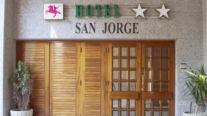 A hotel entrance with a sign reading "HOTEL SAN JORGE," featuring a large wooden door with glass panels and two potted plants on either side. - Hotel San Jorge (Santurtzi)