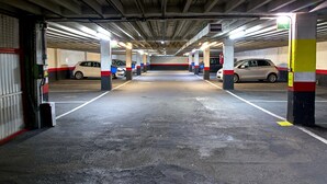 A multi-level parking garage with concrete pillars, marked parking spaces, and overhead lighting. - Hotel San Jorge (Santurtzi)