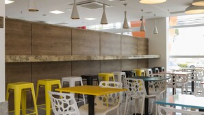 Un interno di un caffè moderno con diverse zone di seduta, inclusi sedie gialle e bianche e tavoli di varie forme e dimensioni.