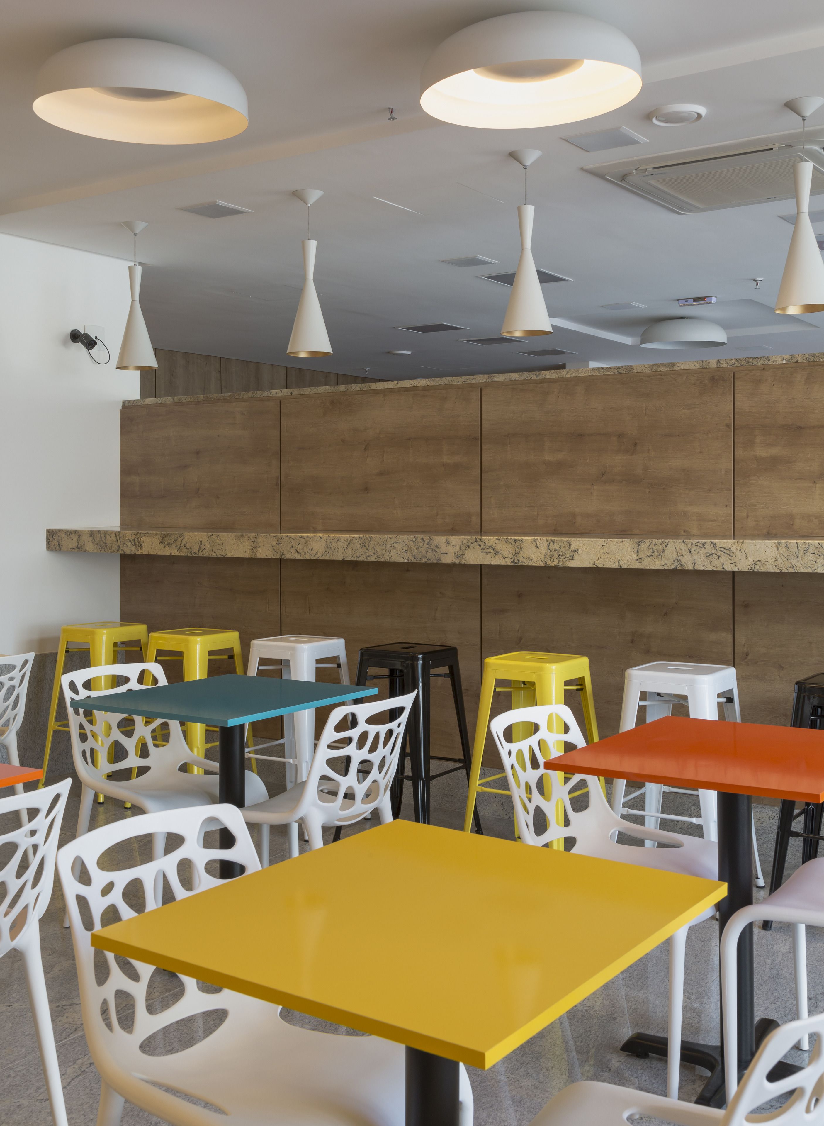 Un interior moderno con varias mesas y sillas, que presenta una variedad de colores y una pared de acento de madera.