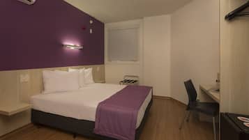 Quarto de hotel com cama, escrivaninha, cadeira e ar condicionado.