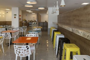 Un comedor moderno con varias mesas y sillas, una cocina al fondo y una barra con taburetes.