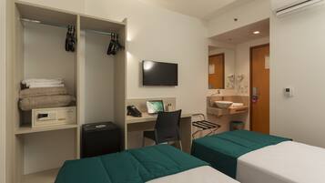 Quarto de hotel com duas camas, uma mesa com computador, televisão, guarda-roupa e banheiro.