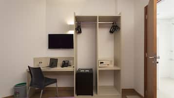Et kompakt hotelværelse med seng, skrivebord med bærbar computer, stol, tv ophængt på væggen, garderobeskab og en lille skraldespand.