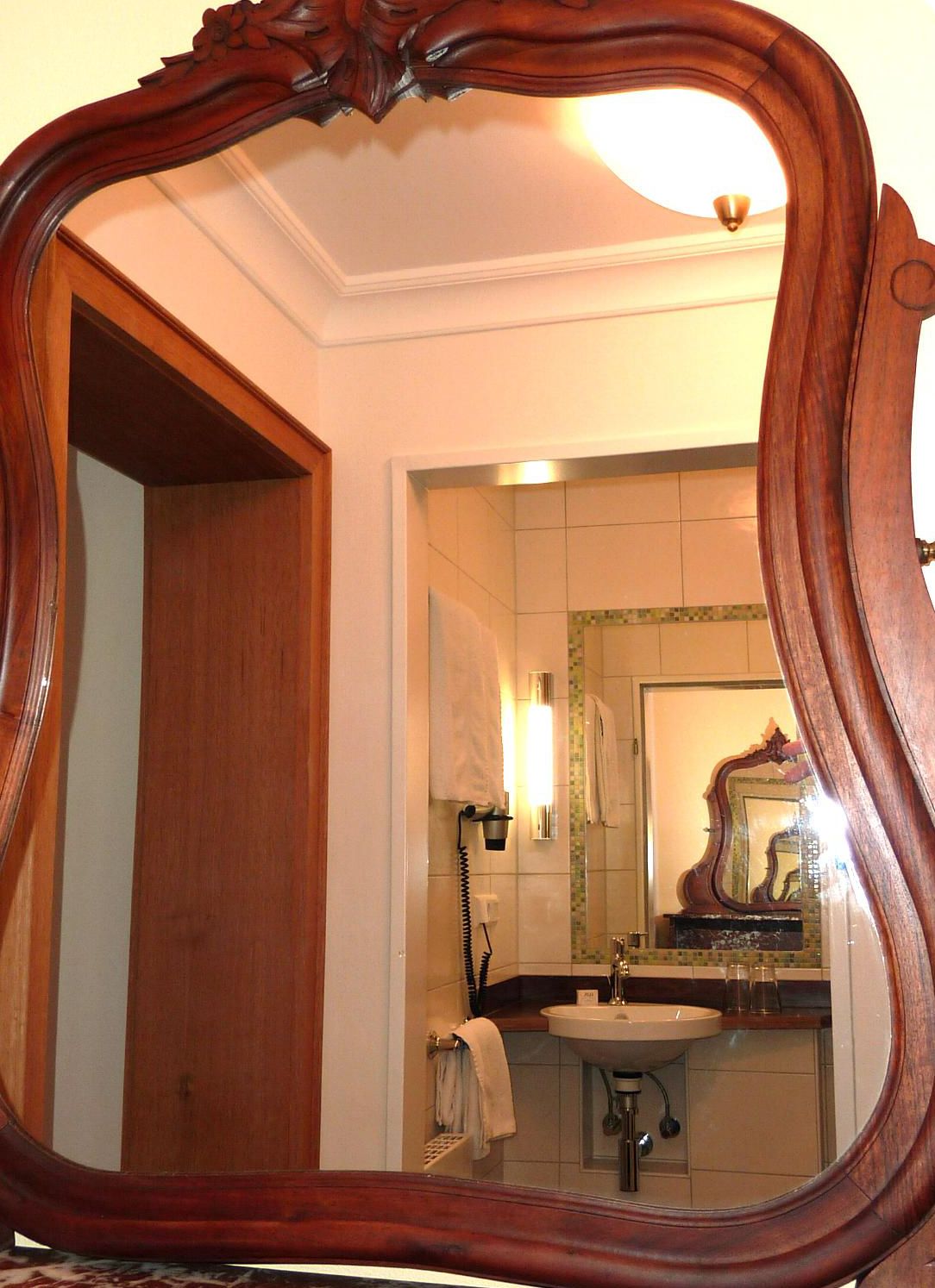 Un baño con un espejo de marco de madera, un lavabo y un perchero para toallas.