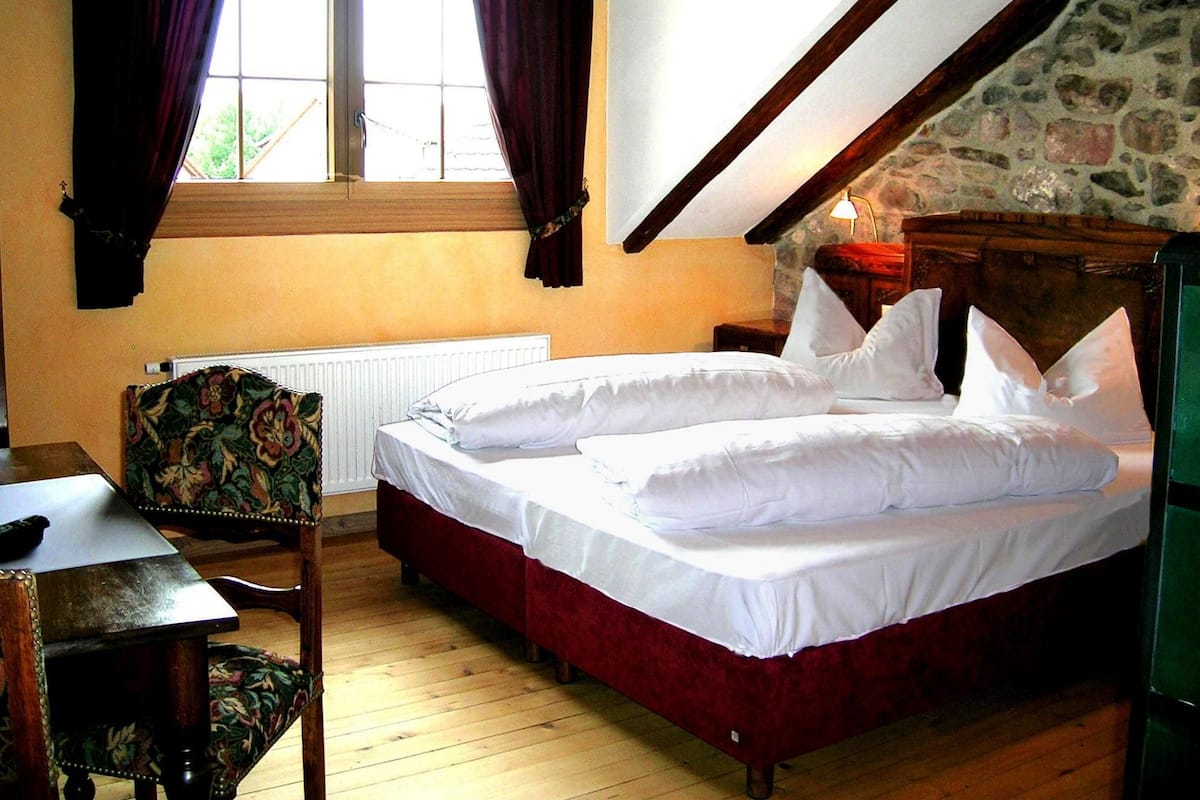 A bedroom with a large bed, a chair, a table, and a window with curtains.