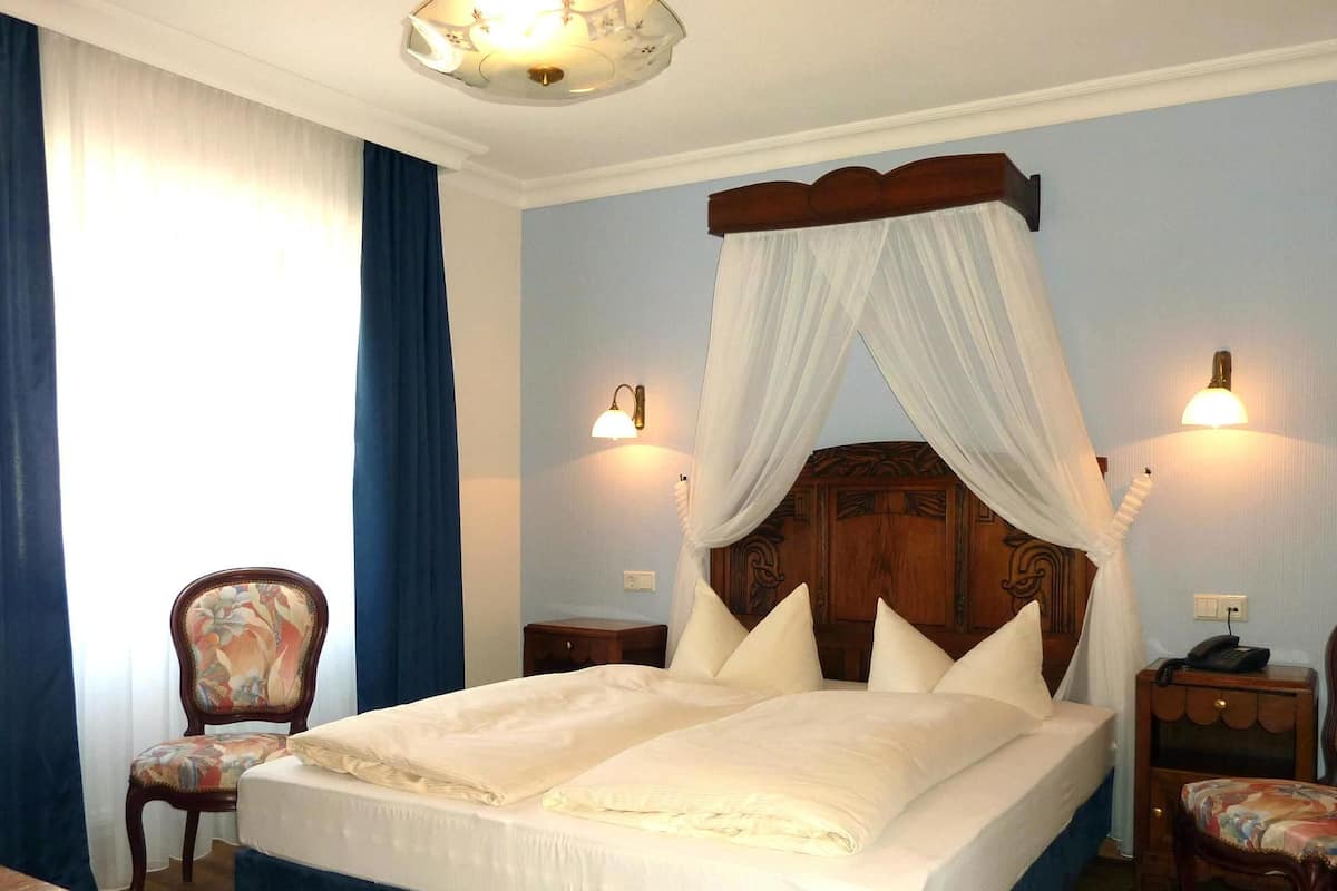 A bedroom with a large bed, a wooden headboard, two bedside tables with lamps, a chair, and a nightstand.