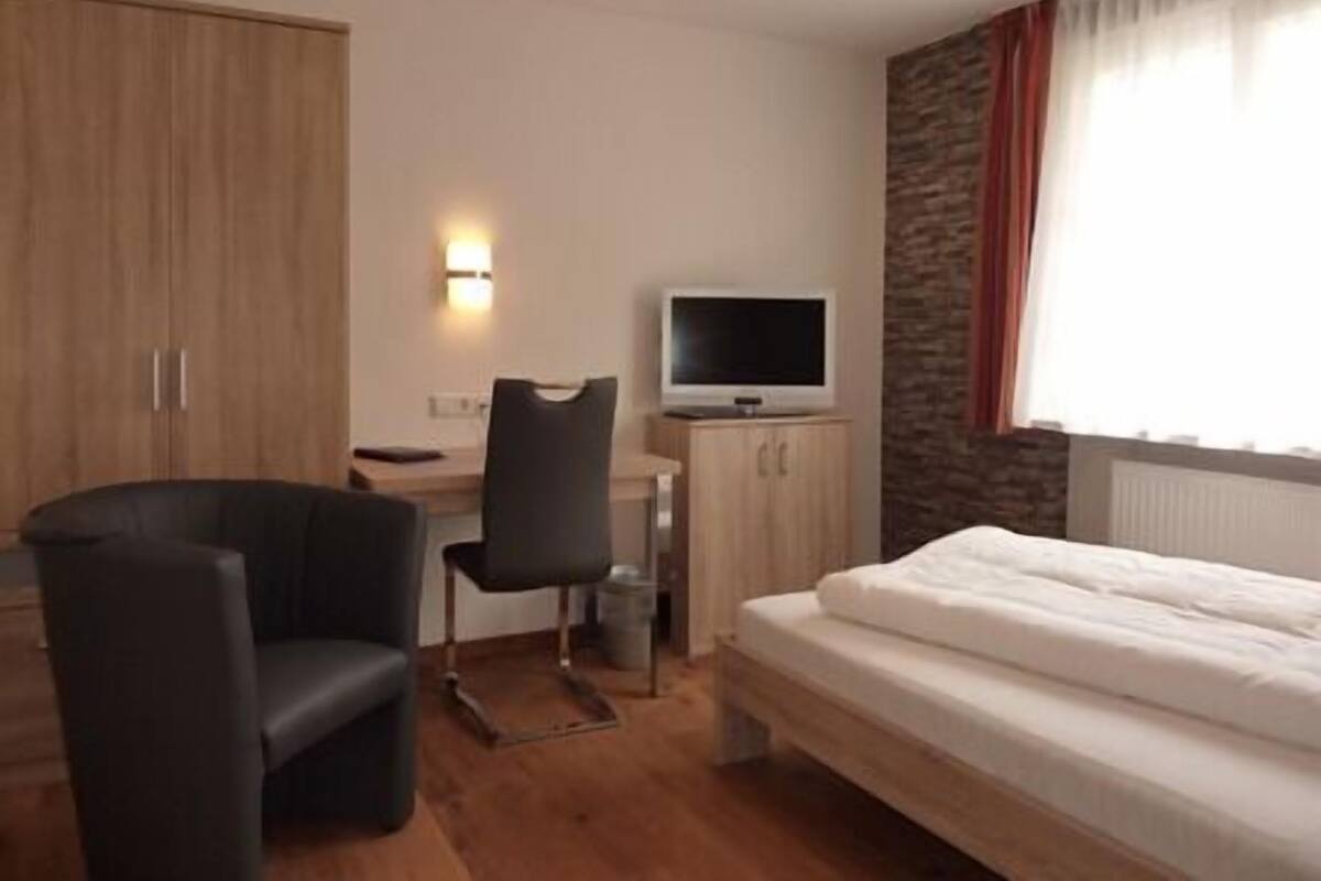 A hotel room with a bed, a desk with a chair, a television, and a wardrobe.