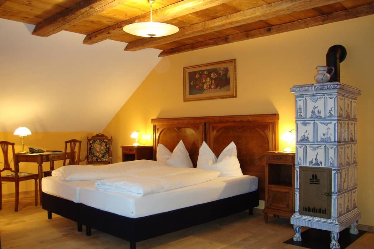 A bedroom with a large bed, wooden headboard, two bedside lamps, a wooden dresser, and a ceiling with exposed beams.