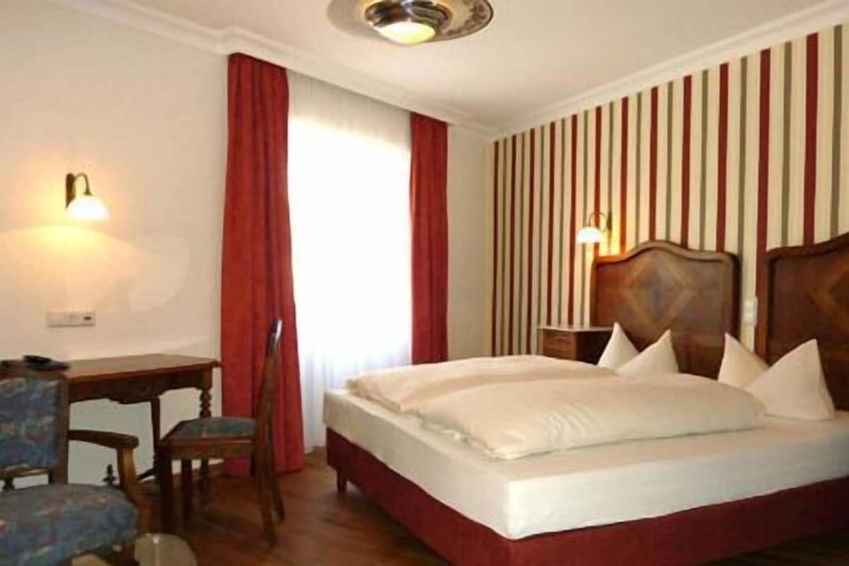 A hotel room with a bed, a desk, a chair, and a lamp.