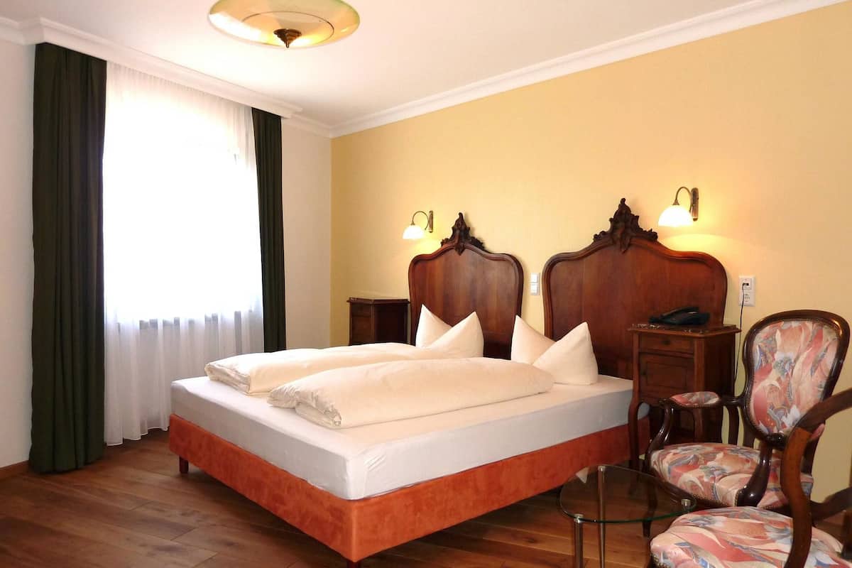 A hotel room with a large bed, two bedside tables, a chair, and a lamp.