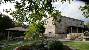 A stone building with a covered patio, a well-maintained garden with a palm tree, and a stone wall. - Casal dos Celenis (Caldas de Reis)
