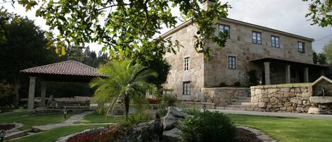 A stone building with a covered patio, a well-maintained garden with a palm tree, and a stone wall.