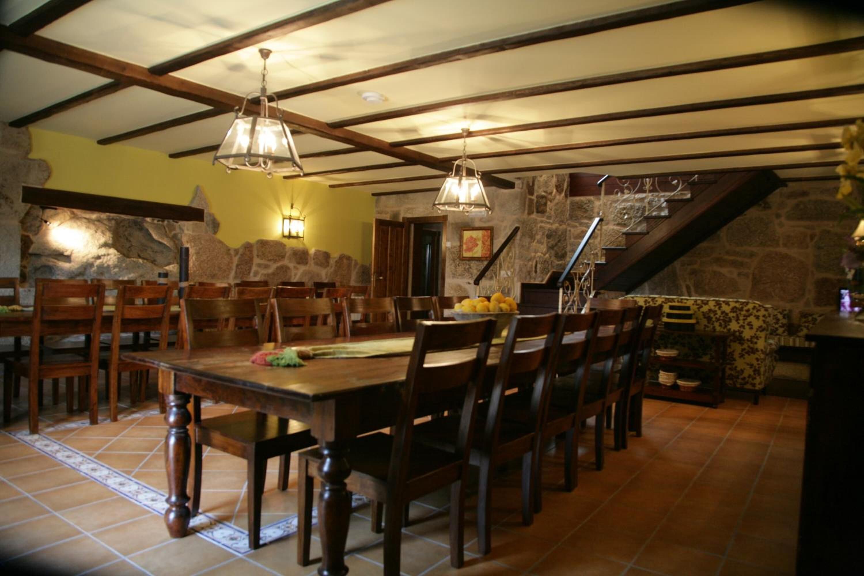 Un espace repas avec une grande table et des chaises en bois, des murs en pierre et un escalier.