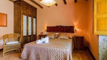 A bedroom with a large bed, wooden wardrobe, wicker chair, and bedside tables with lamps.
