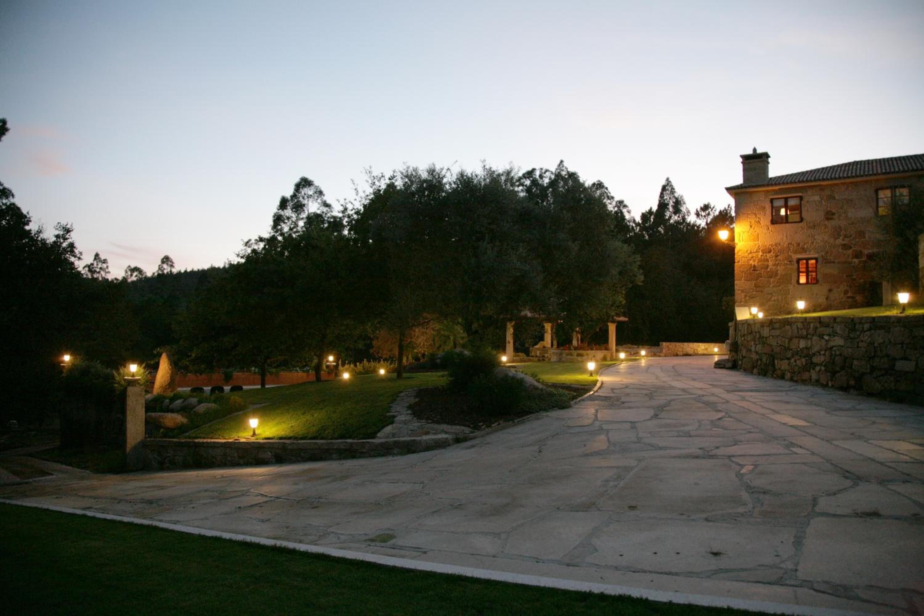Un sendero de piedra conduce a un edificio de piedra con ventanas iluminadas y un césped cuidado.