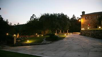 Un sendero de piedra conduce a un edificio de piedra con ventanas iluminadas y un césped cuidado.
