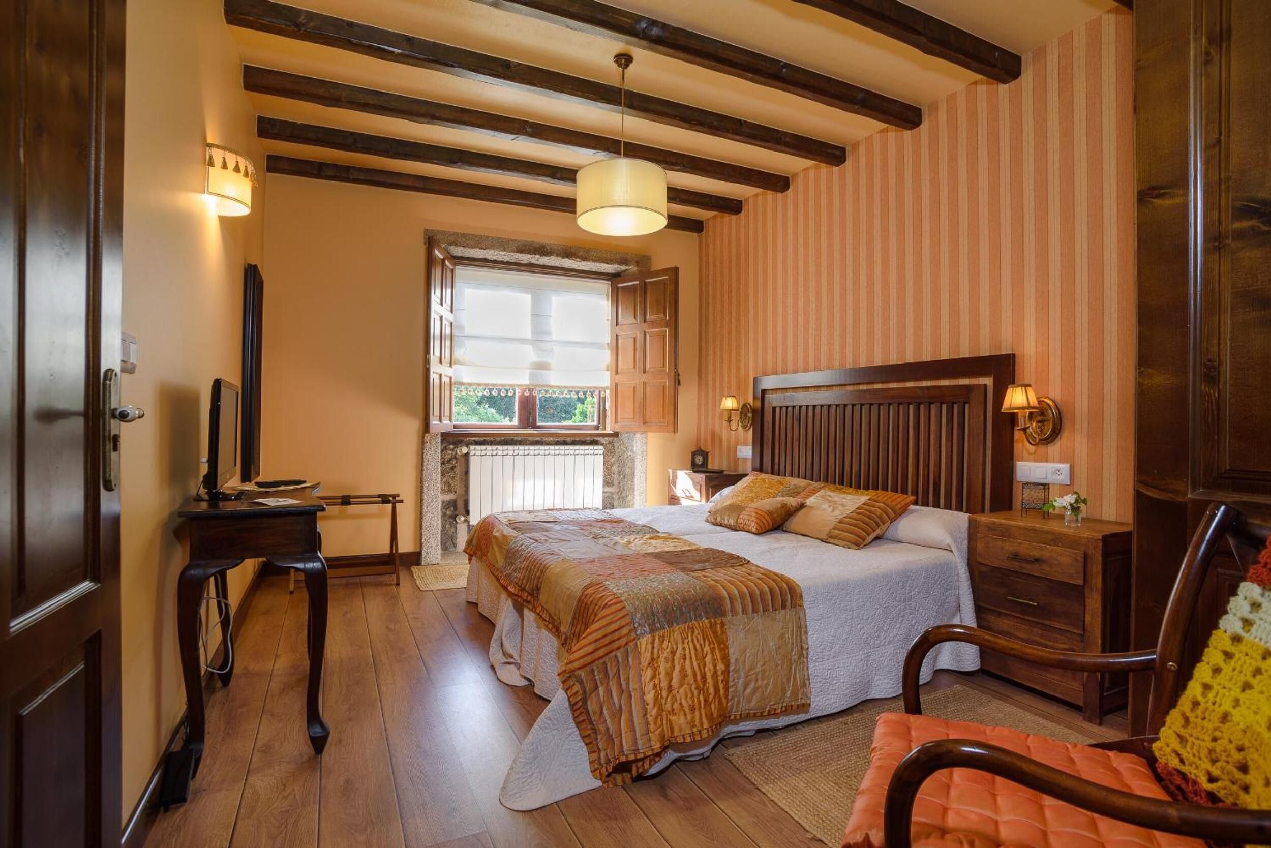 Quarto com uma cama grande, cabeceira de madeira, abajures, uma janela com vista e piso de madeira.