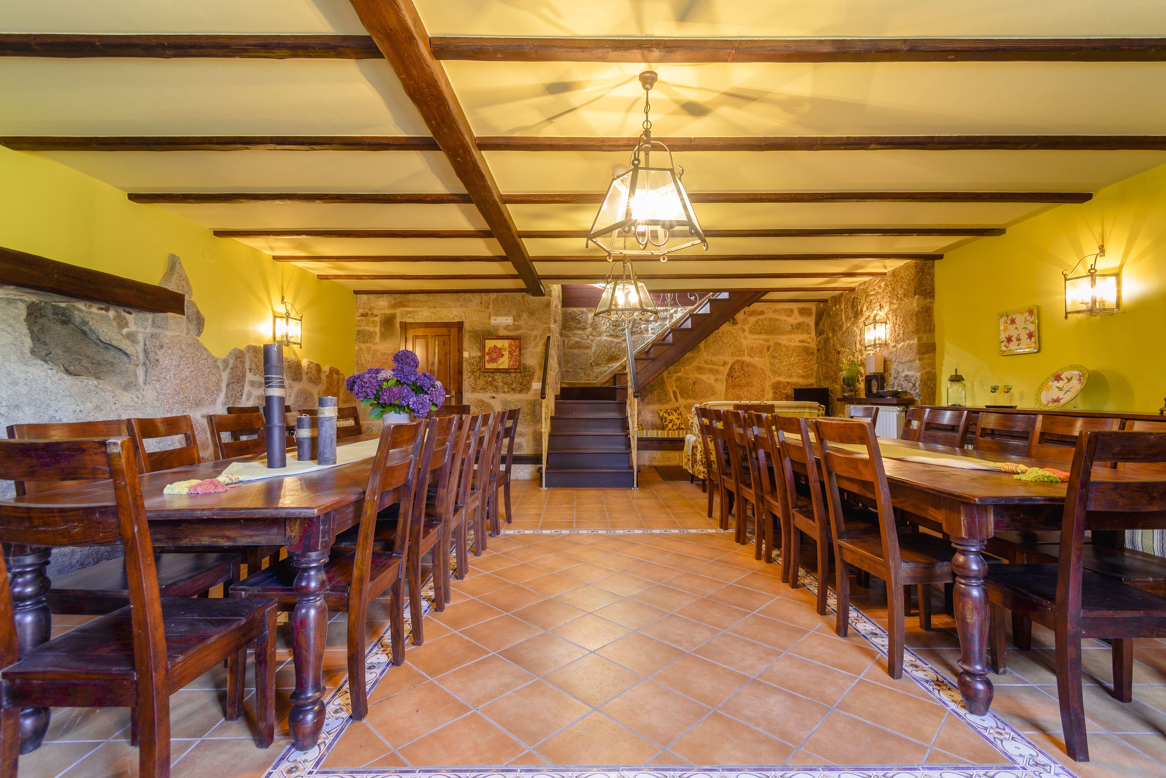 A dining area with wooden tables and chairs, a stone wall, and a staircase leading to an upper level.