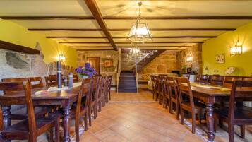 A dining area with wooden tables and chairs, a stone wall, and a staircase leading to an upper level.