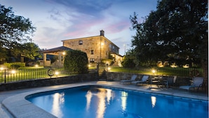 A stone building with a swimming pool, outdoor seating, and a well-lit patio area. - Casal dos Celenis (Caldas de Reis)