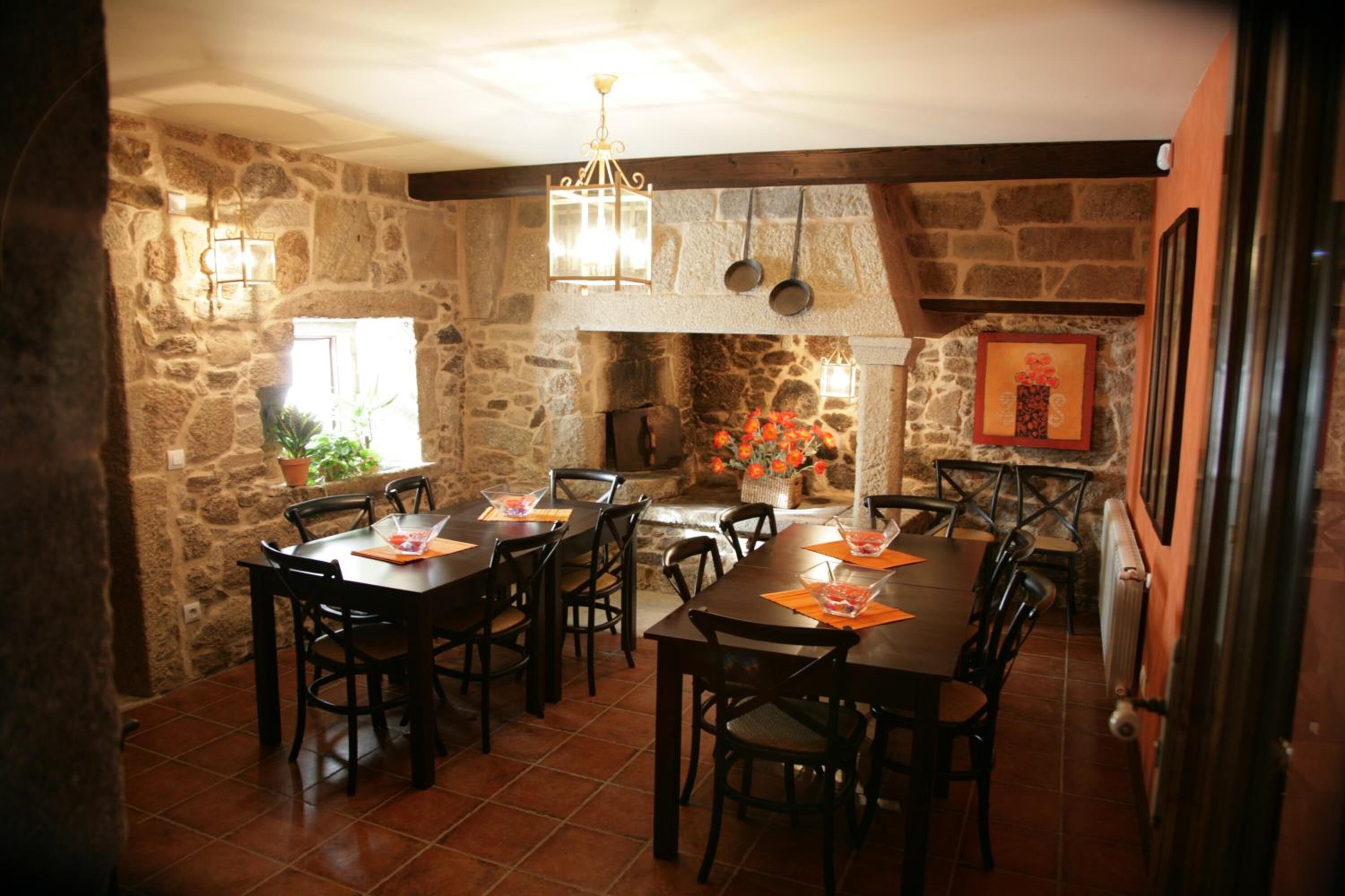 Un comedor rústico con paredes de piedra, mesas y sillas de madera. Hay luces colgantes y una chimenea.