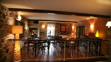 A dining area with stone walls, a wooden ceiling, and a wrought iron railing.