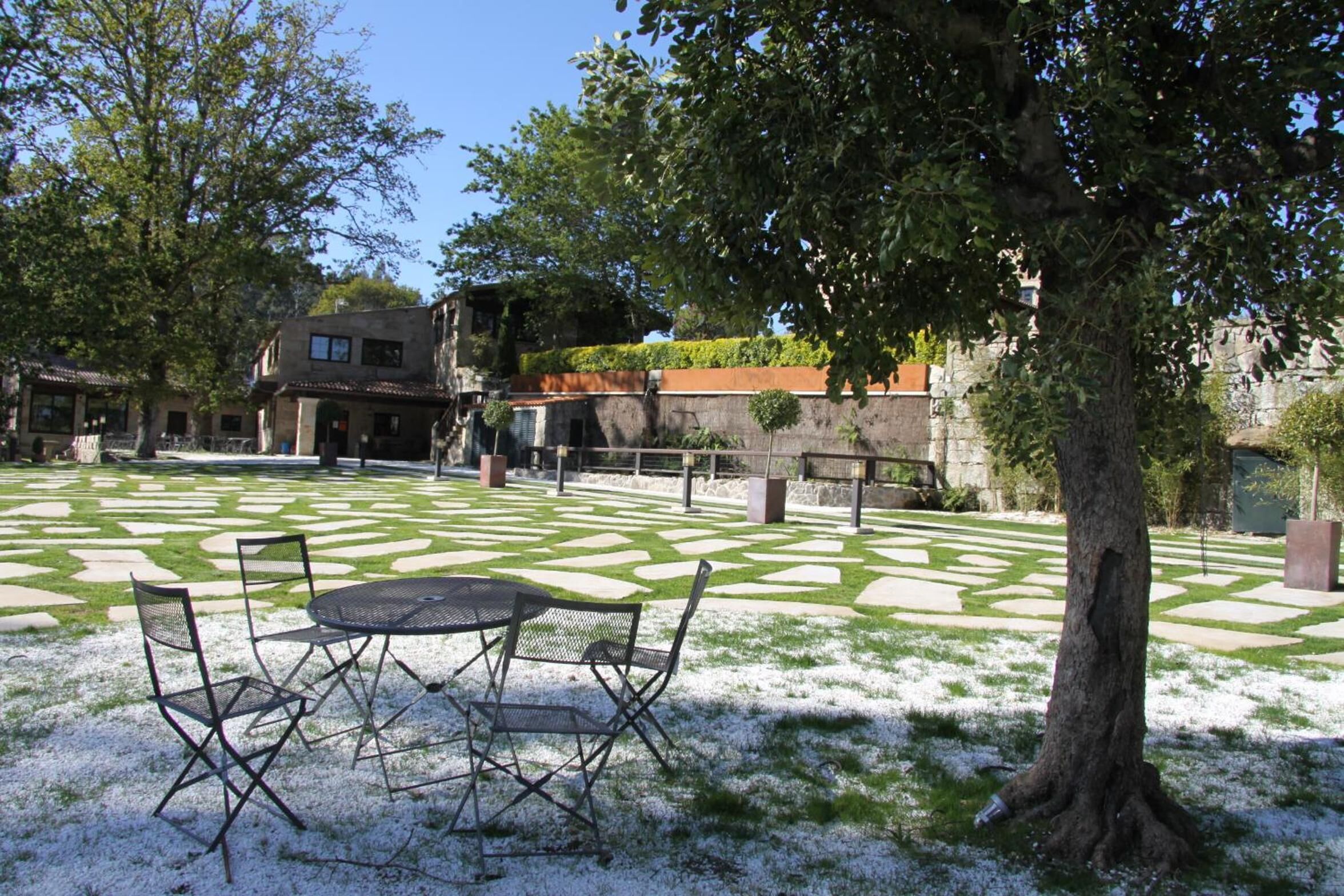 Un patio al aire libre con césped estampado, una mesa metálica con sillas y un árbol.
