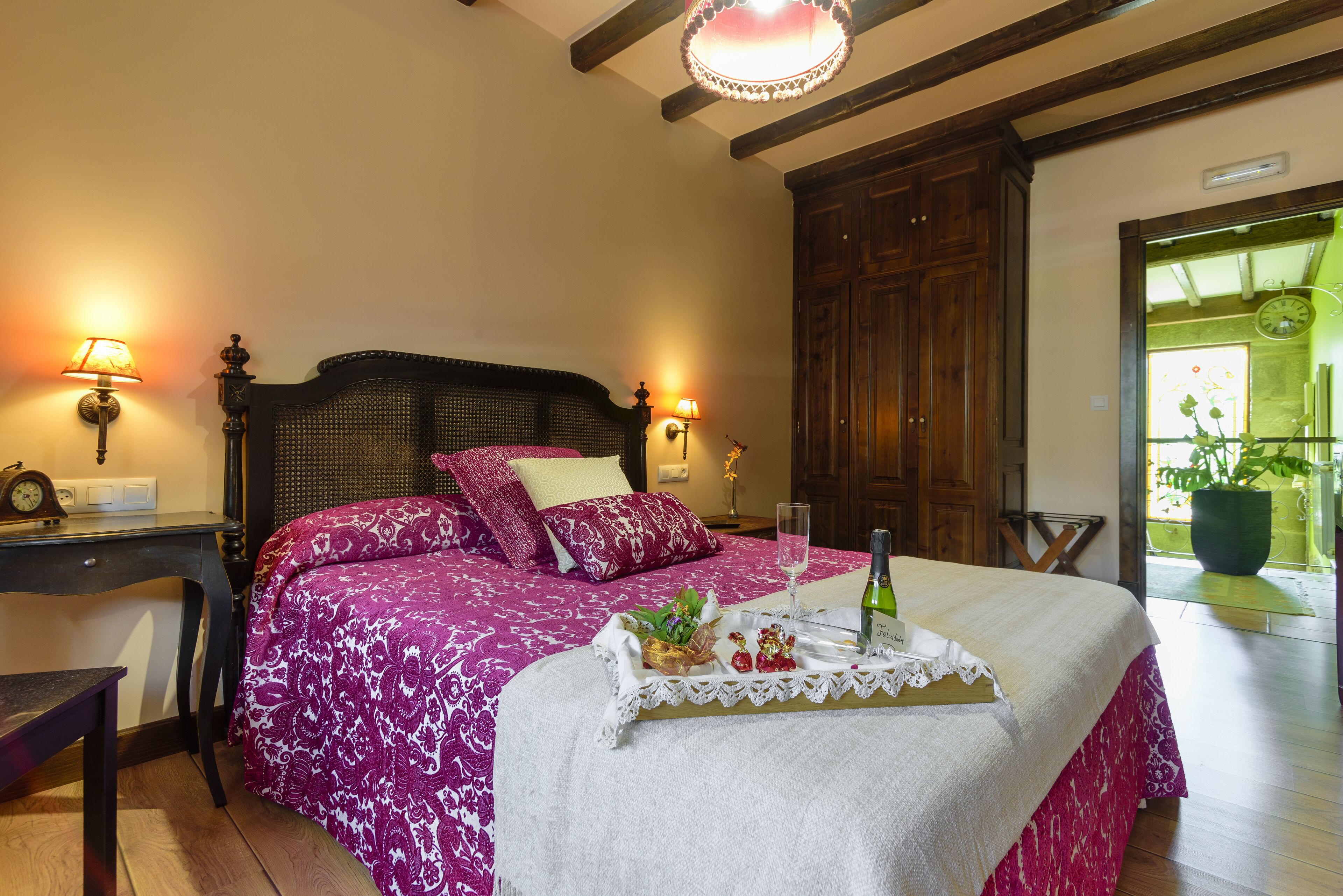 Un dormitorio con cama, lámparas de noche, un armario de madera y una mesita con una botella y vasos.