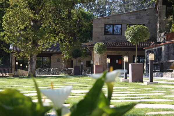 Un patio con un edificio de piedra, un árbol y un césped bien cuidado.